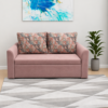 Blush-pink Rube sofa cum bed with patterned cushions displayed in a modern living room with abstract wall art, a potted plant, and a geometric rug.