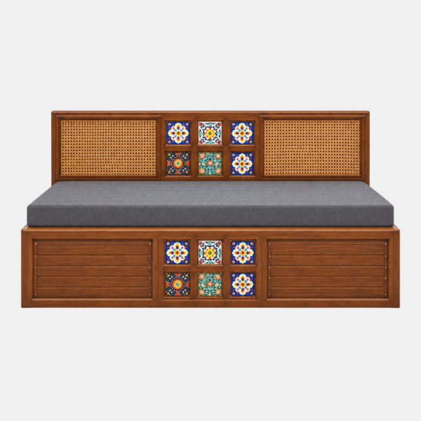 Front view of the Crest Diwan Cum Bed featuring a warm brown wooden frame, decorative cane panels, colourful tile accents, and a grey mattress against a white background.